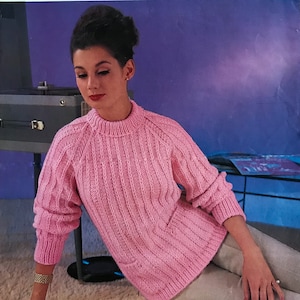 Può includere: Un maglione rosa lavorato a maglia con una trama a coste e un collo rotondo. Il maglione è progettato per adattarsi a misure di busto di 86, 91 o 97 cm.