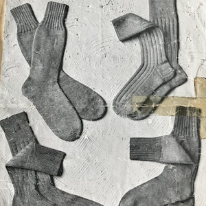 May include: Vintage advertisement featuring several pairs of gray knitted socks. The socks have ribbed cuffs and are displayed in various orientations. The text includes "MEN'S KNITTED SOCKS" and "PATONS & BALDWINS".