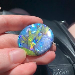 Peut inclure: Un bouton rond avec une image holographique d'un dragon vert et bleu sur fond blanc.