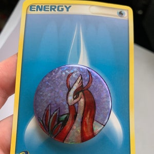 Könnte beinhalten: Eine holografische Pokémon-Karte mit einem roten und weißen Pokémon auf einem violetten Hintergrund. Die Karte ist mit "ENERGIE" beschriftet und hat den Text "SPN-3D2-6AM ©2003 Pokémon/Nintendo 106/109" unten.
