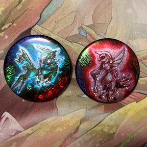 May include: Two round, iridescent buttons featuring Pokemon characters. The left button has a blue and green Pokemon with a red background. The right button has a pink Pokemon with a red background.