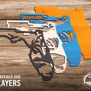 May include: Four layered SVG cut files of the state of Florida with palm trees. The layers are orange, blue, white, and black. The design is titled "3D Layered SVG 4 Layers" and includes the logo "Oceans Apart Graphic Design".