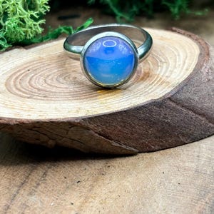 Könnte beinhalten: Ein silberner Ring mit einem blauen Opal-Edelstein. Der Ring liegt auf einer Holzoberfläche.