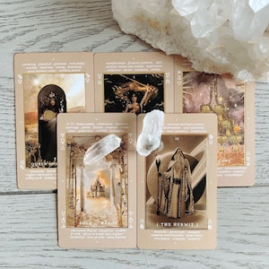 May include: Five tarot cards on a light wood surface with a clear quartz crystal. The cards are from the "Mystic Mondays" deck and feature illustrations of the Queen of Swords, Four of Wands, The Hermit, and the Ten of Cups. The cards are in a beige color with gold accents.