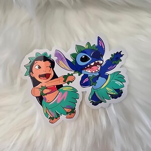 Puede incluir: Dos pegatinas de dibujos animados de Stitch y Lilo de la pel&iacute;cula de Disney Lilo & Stitch. Stitch es azul y lleva un collar de flores verde y una falda de hierba. Lilo lleva una camiseta roja y una falda de hierba verde con detalles rosas y morados.