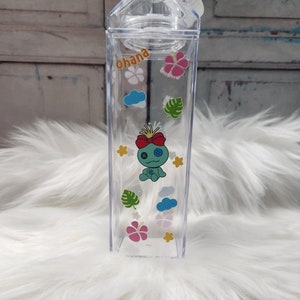 Puede incluir: Botella de agua de pl&aacute;stico transparente, con forma de cart&oacute;n de leche, con tap&oacute;n blanco. Decorada con pegatinas coloridas de un personaje de dibujos animados, flores, nubes y la palabra "ohana".