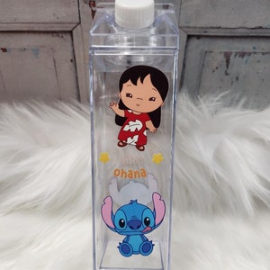 Puede incluir: Botella de agua de pl&aacute;stico transparente con tapa blanca. La botella presenta gr&aacute;ficos de dibujos animados de Lilo y Stitch, con la palabra "Ohana" en amarillo. La botella es rectangular y parece estar vac&iacute;a.