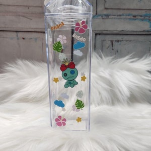 Puede incluir: Botella de agua de pl&aacute;stico transparente con forma de cart&oacute;n de leche, con tapa blanca. Decorada con gr&aacute;ficos de dibujos animados de una criatura azul, flores, nubes y la palabra "ohana".