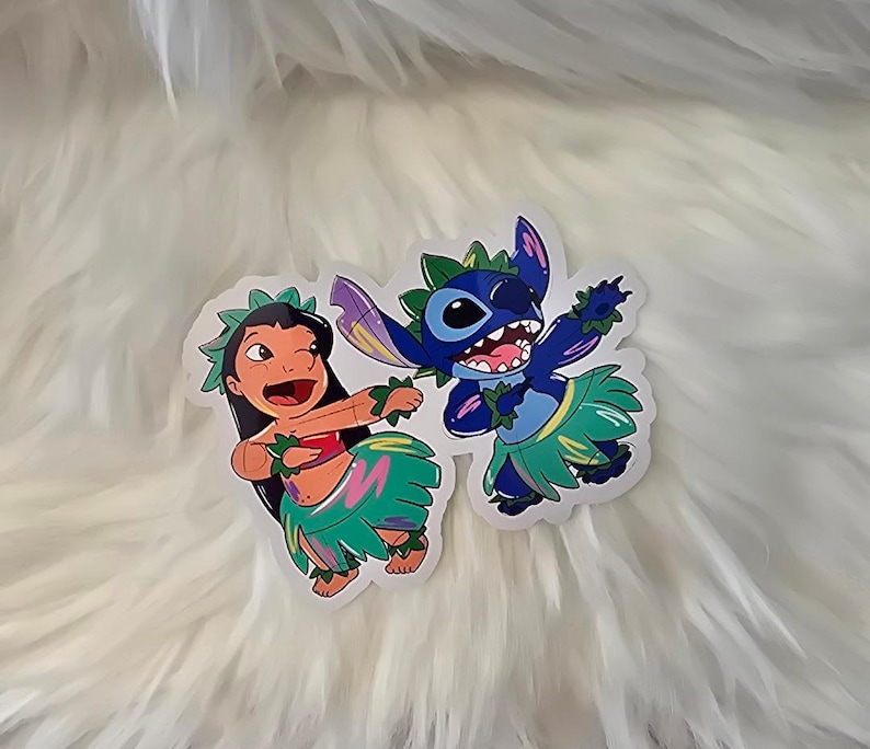 Puede incluir: Dos personajes de dibujos animados, Stitch y Lilo, est&aacute;n vestidos con faldas de hula y collares de flores. Stitch es azul con tres dedos en cada mano y lleva un collar de flores verde. Lilo lleva una camiseta roja y un collar de flores verde.