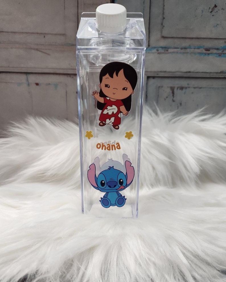 Puede incluir: Botella de agua de pl&aacute;stico transparente con tapa blanca, con los personajes de dibujos animados Lilo y Stitch. La botella tiene forma rectangular y la palabra "Ohana" impresa, con estrellas amarillas.