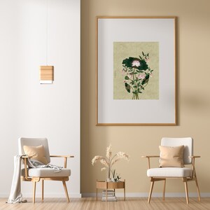 May include: A framed print of a botanical illustration featuring a pink flower with green leaves on a beige background. The print is hanging on a beige wall in a room with two chairs and a side table.