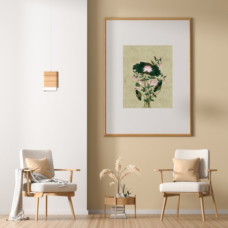 May include: A framed print of a botanical illustration featuring a pink flower with green leaves on a beige background. The print is hanging on a beige wall in a room with two chairs and a side table.