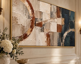 May include: A large rectangular abstract painting in a gold frame featuring a textured composition of geometric blocks and circular arcs in shades of navy blue, burnt orange, cream, and gray, displayed on a wall above a marble console table.