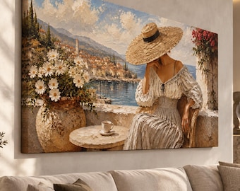 May include: A large rectangular canvas wall art print depicting a person wearing a wide-brimmed straw hat and a long dress, sitting at a small table with a cup of coffee. A large stone vase filled with white daisies sits beside a coastal town view.