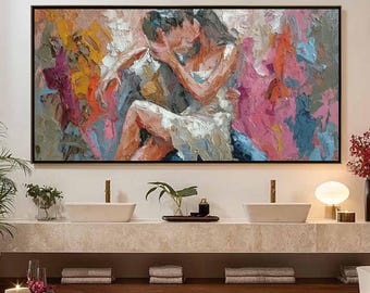May include: An abstract painting in a black frame depicts a couple embracing in a passionate kiss. The artwork uses thick brushstrokes and a palette of pink, orange, blue, and white to create a textured effect. The painting is displayed above a bathroom vanity.
