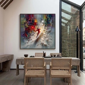 Puede incluir: Pintura al &oacute;leo abstracta en un marco negro. La obra presenta a un esquiador con un traje rojo, sobre un fondo texturizado y colorido con tonos blancos, rojos, amarillos y azules. La pintura est&aacute; sobre una mesa de comedor.
