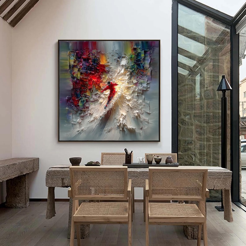 Puede incluir: Pintura al &oacute;leo abstracta en un marco negro. La obra presenta a un esquiador con un traje rojo, sobre un fondo texturizado y colorido con tonos blancos, rojos, amarillos y azules. La pintura est&aacute; sobre una mesa de comedor.