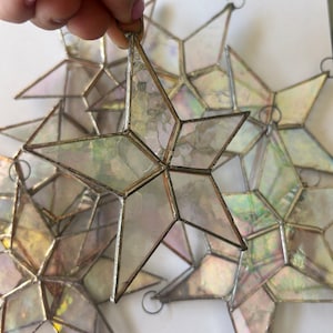 May include: A set of iridescent glass star ornaments with silver wire hangers. The stars are made of clear glass with a rainbow iridescent finish.