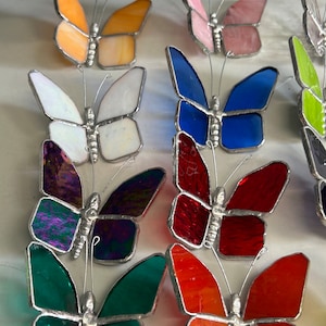 Pu&ograve; includere: Una collezione di farfalle in vetro colorato, tra cui arancione, bianco, blu, rosso, verde e viola. Le farfalle sono fatte di vetro e hanno una struttura in filo metallico.