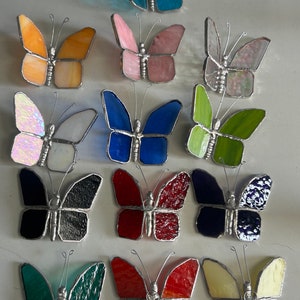 Pu&ograve; includere: Assortimento di farfalle in vetro colorato in vari colori, tra cui blu, rosa, verde, rosso, nero e giallo. Le farfalle sono tutte di dimensioni approssimativamente uguali e hanno un design simile.
