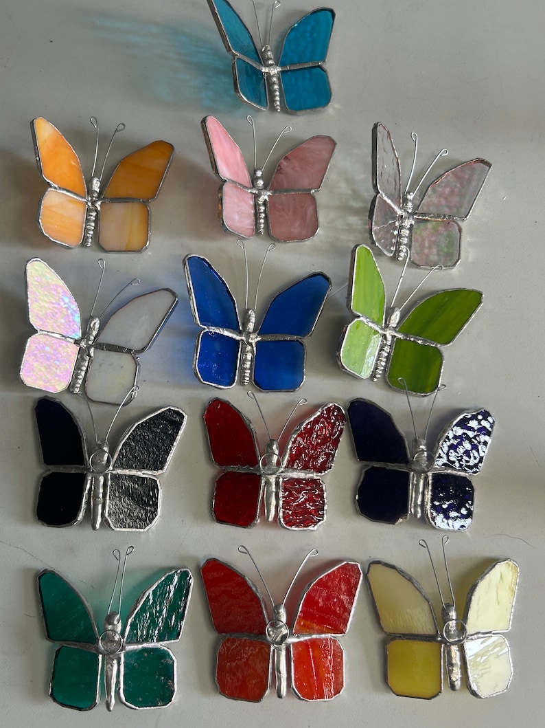 Pu&ograve; includere: Assortimento di farfalle in vetro colorato in vari colori, tra cui blu, rosa, verde, rosso, nero e giallo. Le farfalle sono tutte di dimensioni approssimativamente uguali e hanno un design simile.