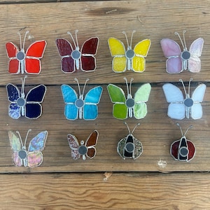Pu&ograve; includere: Assortimento di farfalle e coccinelle in vetro colorato, in vari colori, tra cui rosso, blu, giallo, verde e rosa. Le farfalle e le coccinelle sono tutte in vetro e hanno una finitura metallica.