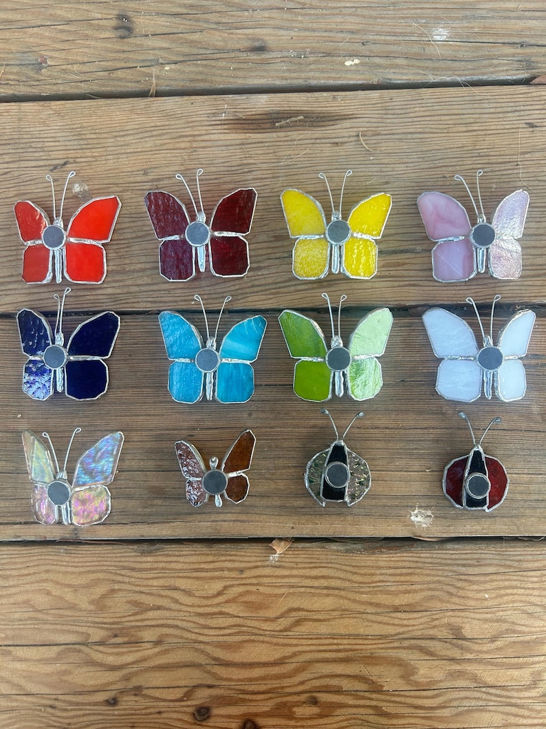 Pu&ograve; includere: Assortimento di farfalle e coccinelle in vetro colorato, in vari colori, tra cui rosso, blu, giallo, verde e rosa. Le farfalle e le coccinelle sono tutte in vetro e hanno una finitura metallica.