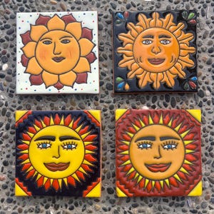 May include: Four square ceramic tiles featuring sun face designs. The top left tile has a yellow sun on white with dots. The top right has a yellow sun on black. The bottom left features a yellow sun on a dark blue background. The bottom right shows a yellow sun on a red background.