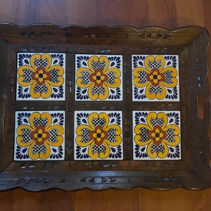 May include: Wooden serving tray with six square ceramic tiles. Each tile features a yellow, orange, and blue floral design. The tray has a dark brown, carved wooden frame with handles on the sides.