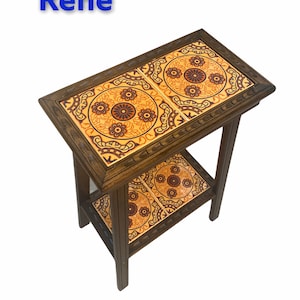 May include: A wooden end table with two shelves. The top shelf has two square tiles with a floral pattern in shades of orange, brown, and yellow. The bottom shelf has one square tile with the same pattern.