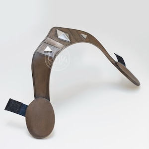 May include: A brown leather headband with silver metal accents. The headband is curved and has a padded section on one side.