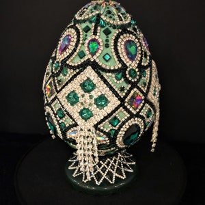 May include: A green egg-shaped decorative object covered in rhinestones and beads. The egg is on a stand and has a geometric design.