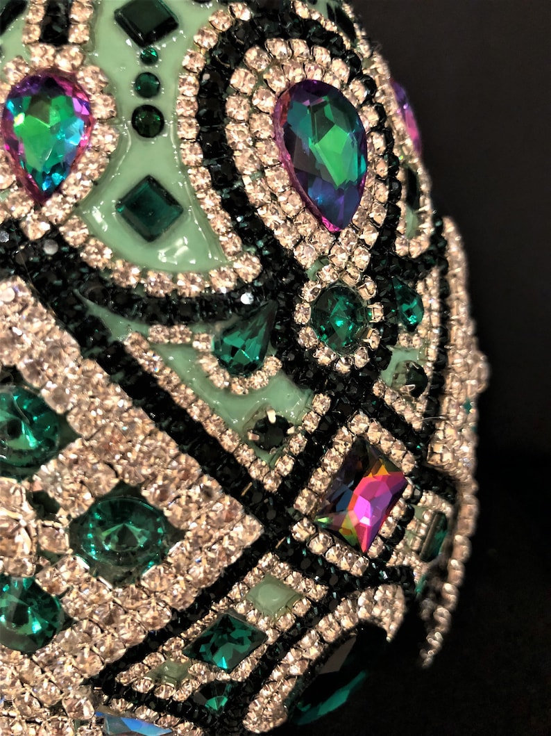 May include: A green egg-shaped object covered in rhinestones and small green and iridescent gems. The object is decorated with a black and white geometric pattern.