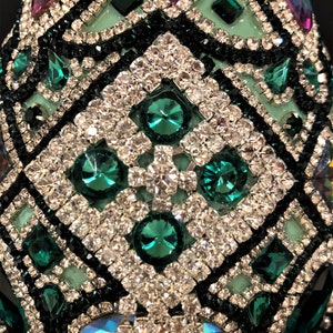 May include: A green and black egg-shaped ornament covered in rhinestones and emerald green jewels. The ornament has a geometric pattern.