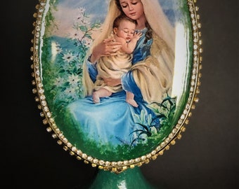 May include: A green musical jewellery box with a gold trim and a white oval picture of Mary holding baby Jesus. The picture is surrounded by a gold trim and rhinestones.