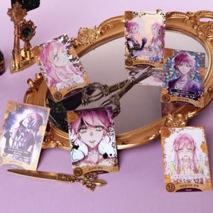 May include: A collection of anime-style character cards with gold foil accents, featuring various characters with pink and purple hair. The cards are arranged around a gold-framed mirror, with a gold-colored decorative knife and other accessories.