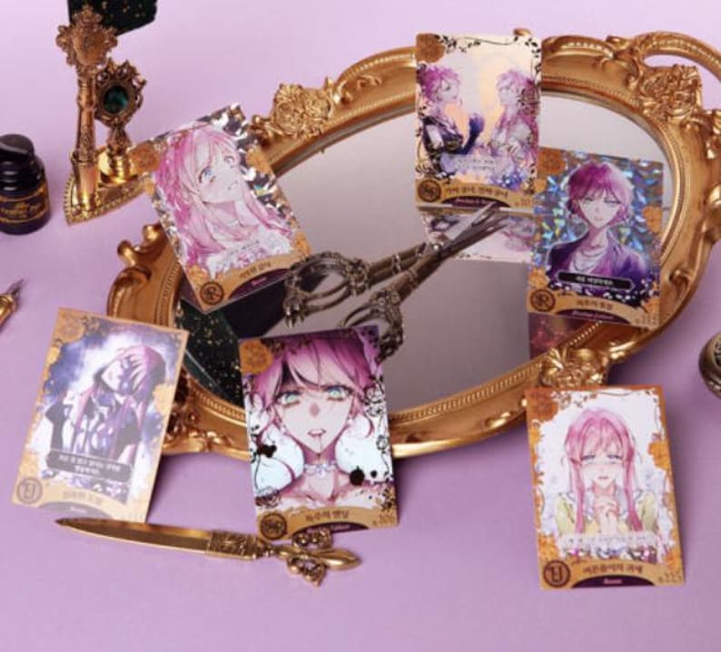 May include: A collection of anime-style character cards with gold foil accents, featuring various characters with pink and purple hair. The cards are arranged around a gold-framed mirror, with a gold-colored decorative knife and other accessories.