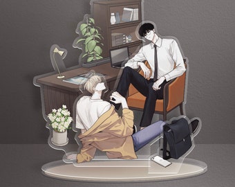 May include: A clear acrylic stand with two figures. The figure on the left is wearing a yellow jacket and jeans. The figure on the right is wearing a white shirt and black pants. The stand has a small potted plant, a desk, and a chair.