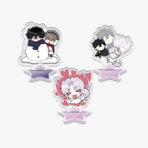 Puede incluir: Tres expositores acrílicos con personajes de estilo anime. Uno muestra dos figuras construyendo un muñeco de nieve, otro representa varios personajes, y el último tiene un personaje rodeado de corazones. Cada expositor tiene una base en forma de estrella.