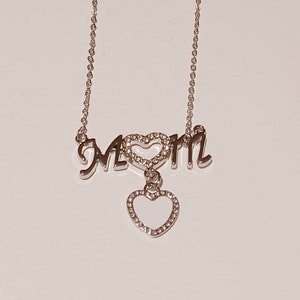 May include: Silver necklace with a charm that says "MOM" with a heart in the middle and a dangling heart charm.