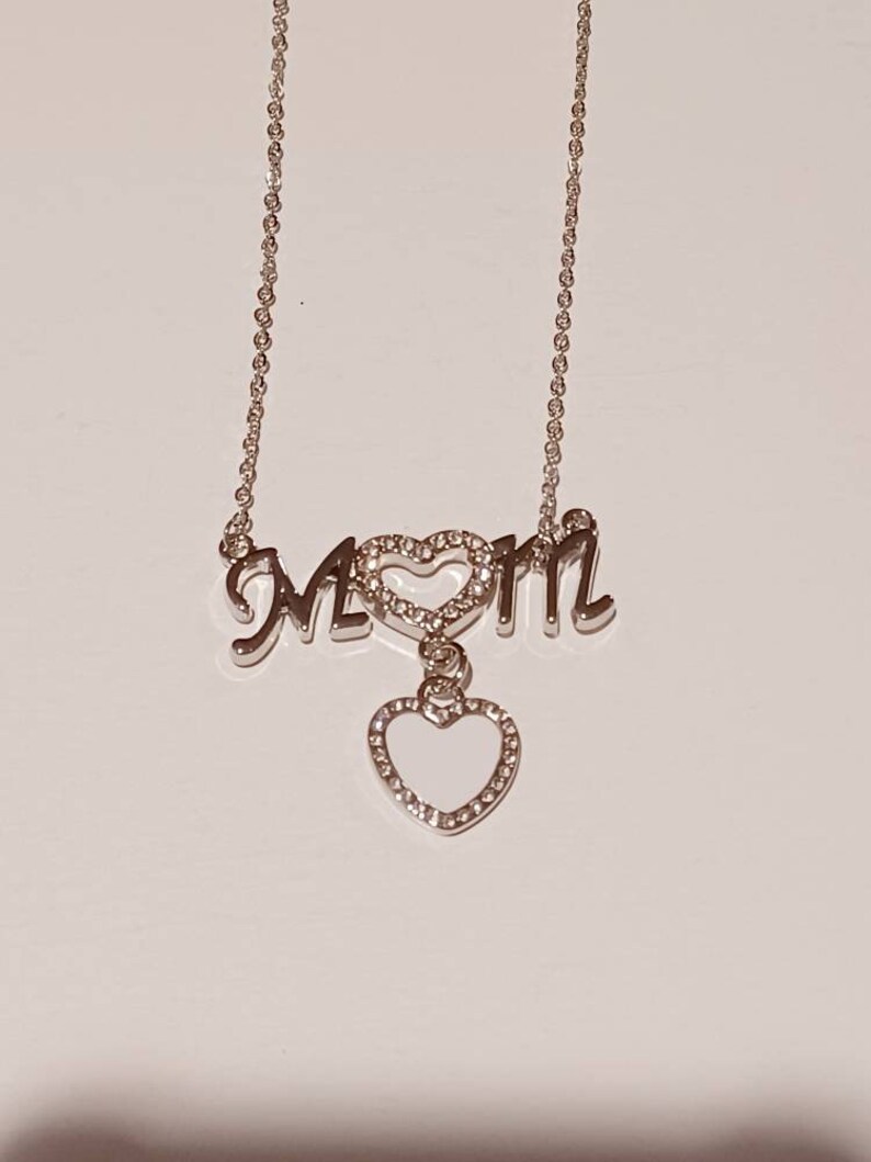 May include: Silver necklace with a charm that says "MOM" with a heart in the middle and a dangling heart charm.
