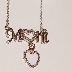 May include: Silver necklace with the word "Mom" spelled out with a heart charm in the middle and a dangling heart charm with white enamel and clear rhinestones.