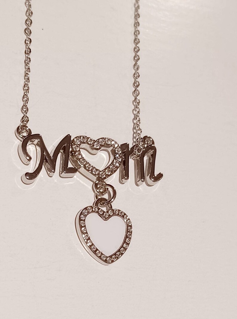 May include: Silver necklace with the word "Mom" spelled out with a heart charm in the middle and a dangling heart charm with white enamel and clear rhinestones.