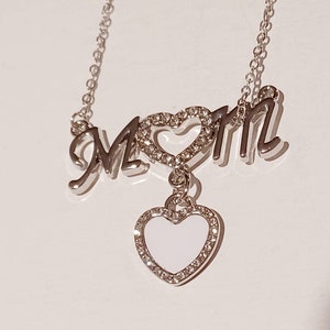 May include: Silver necklace with the word "MOM" spelled out with a heart in the middle. The heart has a smaller heart charm hanging from it.