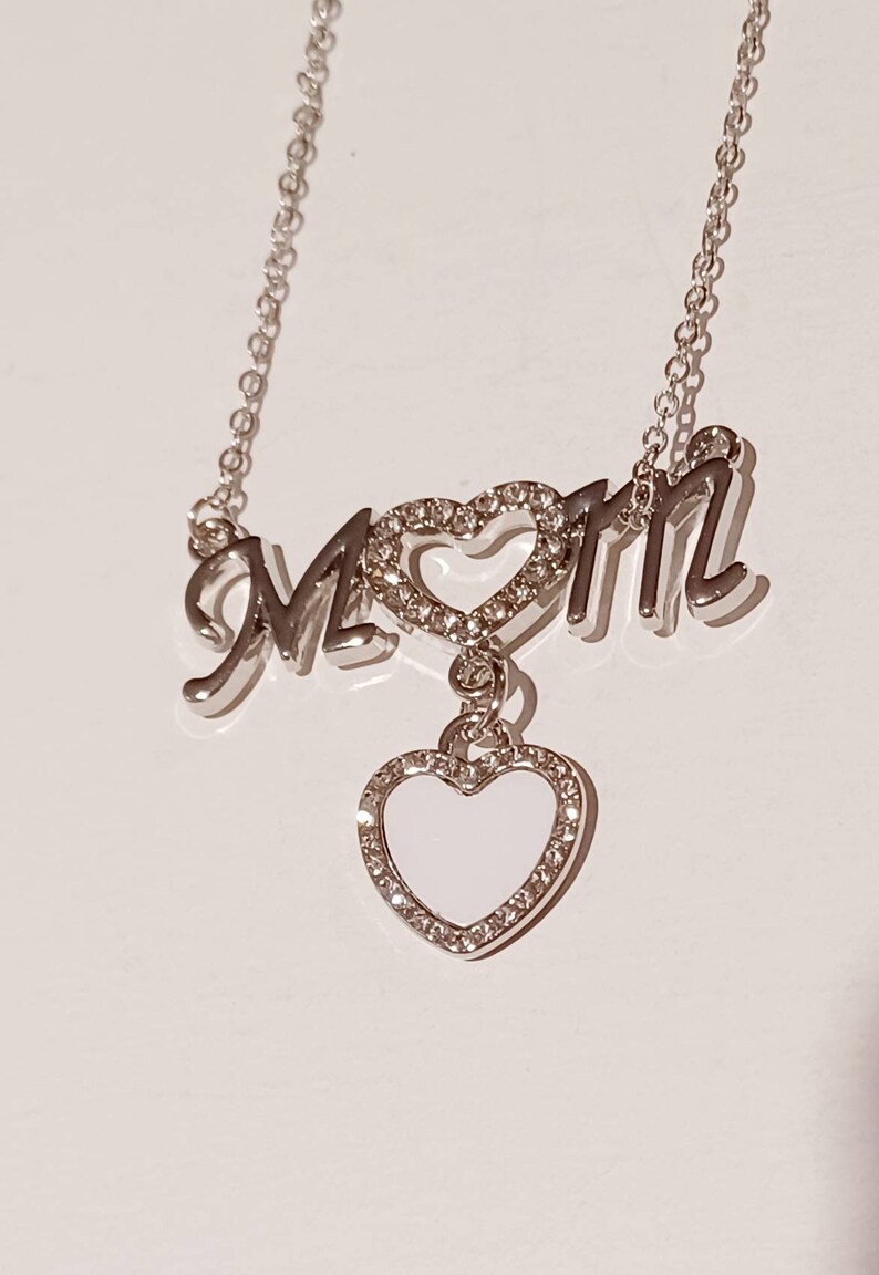 May include: Silver necklace with the word "MOM" spelled out with a heart in the middle. The heart has a smaller heart charm hanging from it.