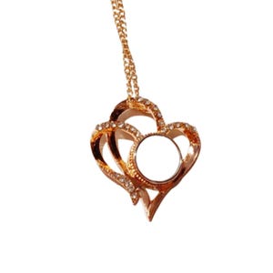 May include: A gold-colored pendant necklace featuring a double heart design. The hearts are adorned with small, clear crystals and surround a circular, open space. The necklace hangs from a delicate gold chain.