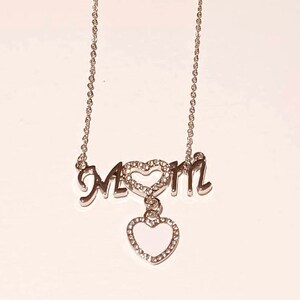 May include: Silver necklace with a pendant that says "MOM" with a heart in the middle and a dangling heart charm.