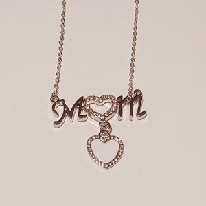 May include: Silver necklace with a charm that says "MOM" with a heart in the middle and a dangling heart charm.