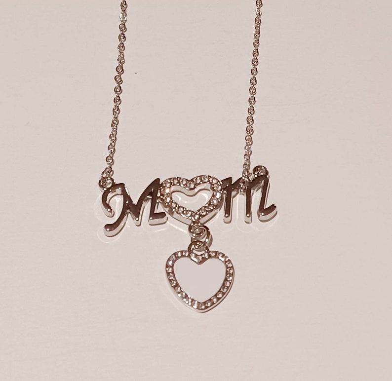 May include: Silver necklace with a charm that says "MOM" with a heart in the middle and a dangling heart charm.