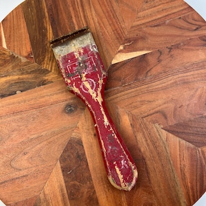 Puede incluir: Un raspador de pintura rojo y dorado con mango de madera. El raspador tiene las palabras "Best Quality" y "Scraper" impresas.